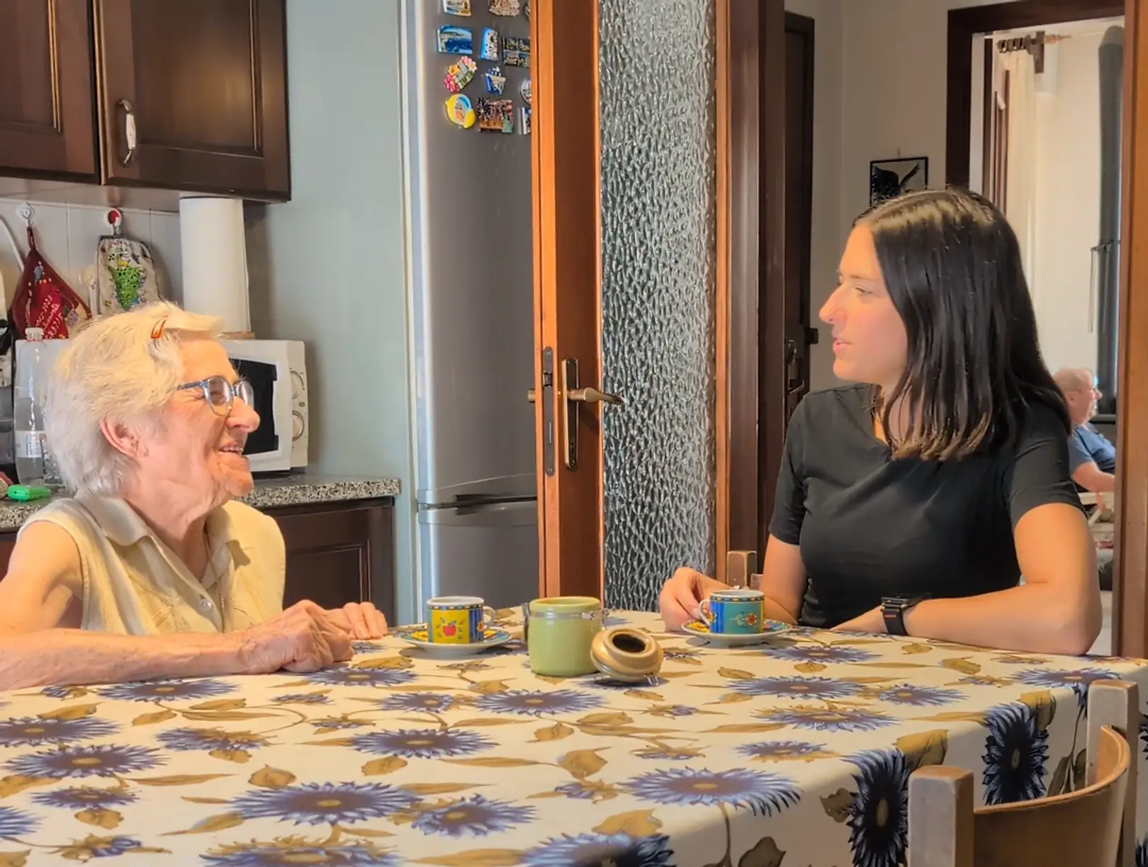 Un'anziana ride mentre prende il caffe' al tavolo di casa con l'operatrice Senilia