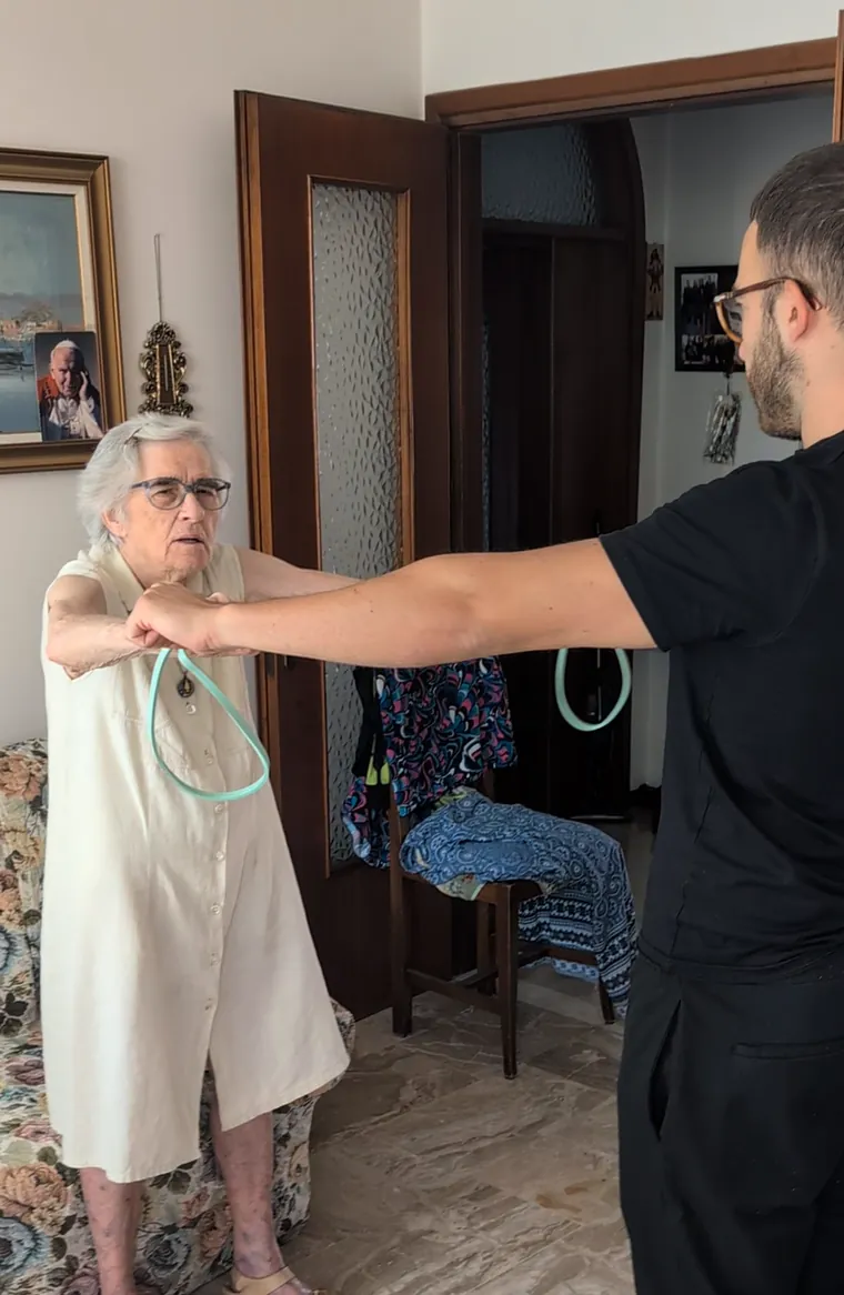 Un'anziana fa esercizi con l'elastico insieme all'operatore Senilia, in soggiorno
