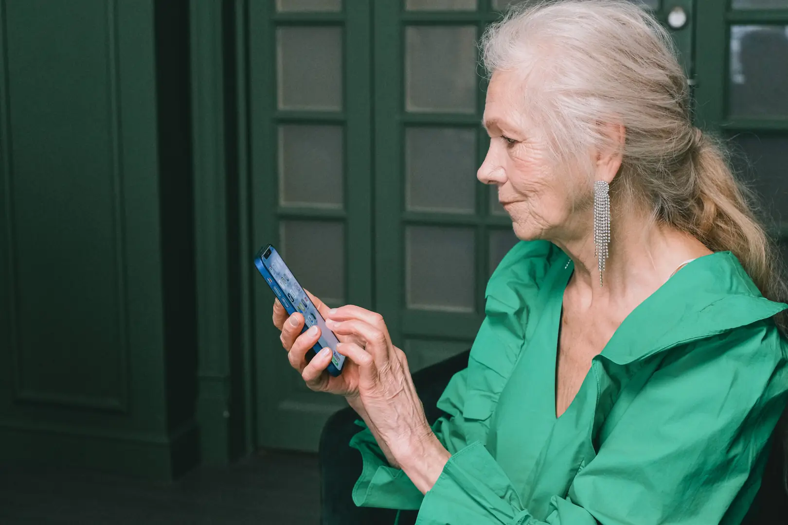 Una signora con i capelli bianchi guarda lo smartphone che tiene in mano