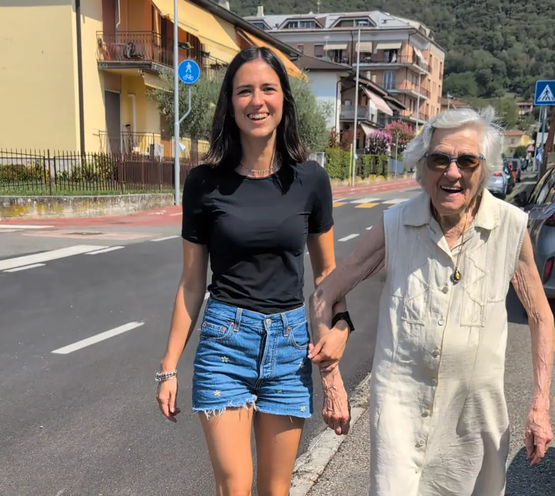 Un’anziana sorridente per strada, tenuta per mano dall’operatrice Senilia