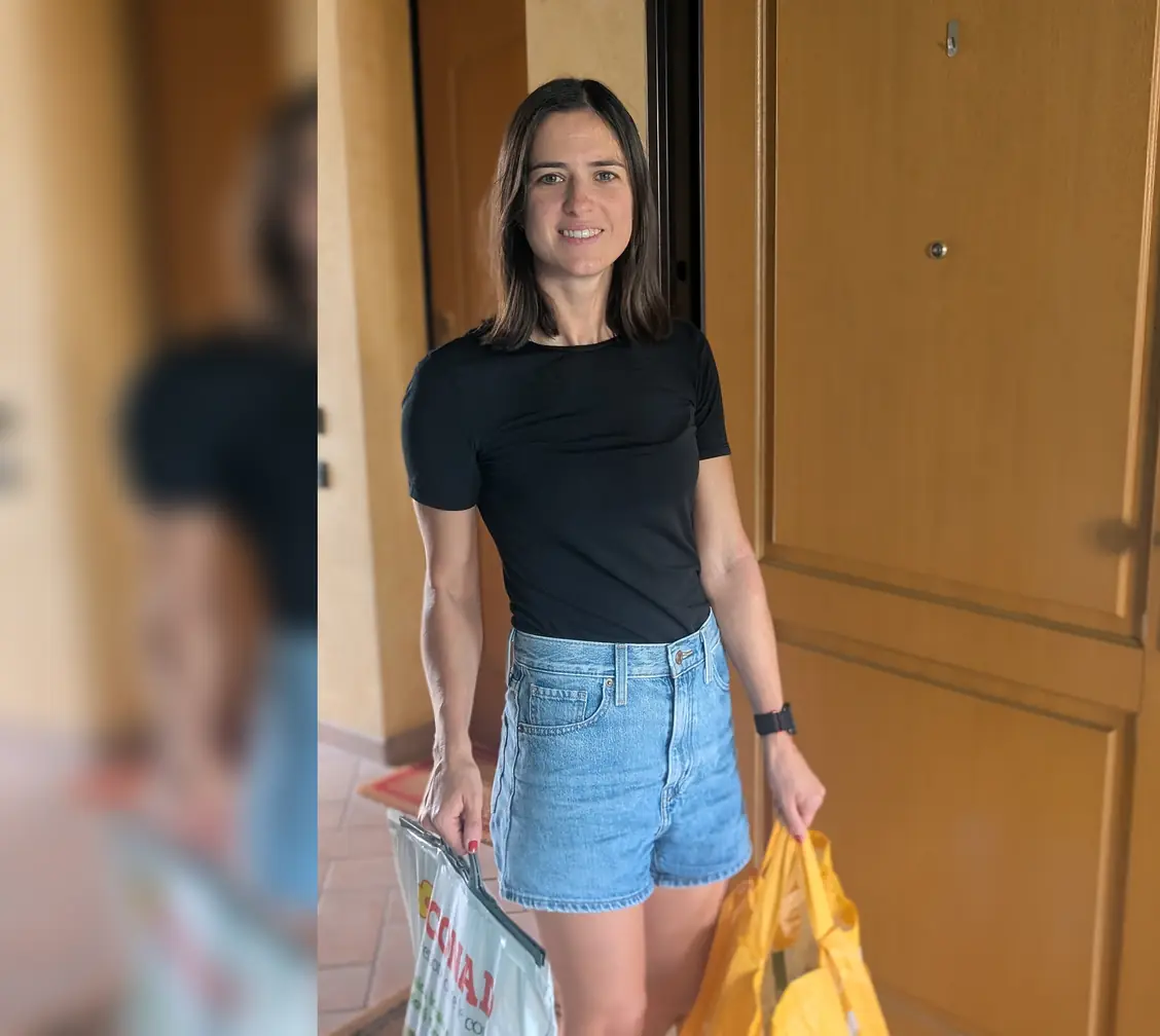 Una ragazza sorridente sulla porta di un appartamento, con la spesa in mano