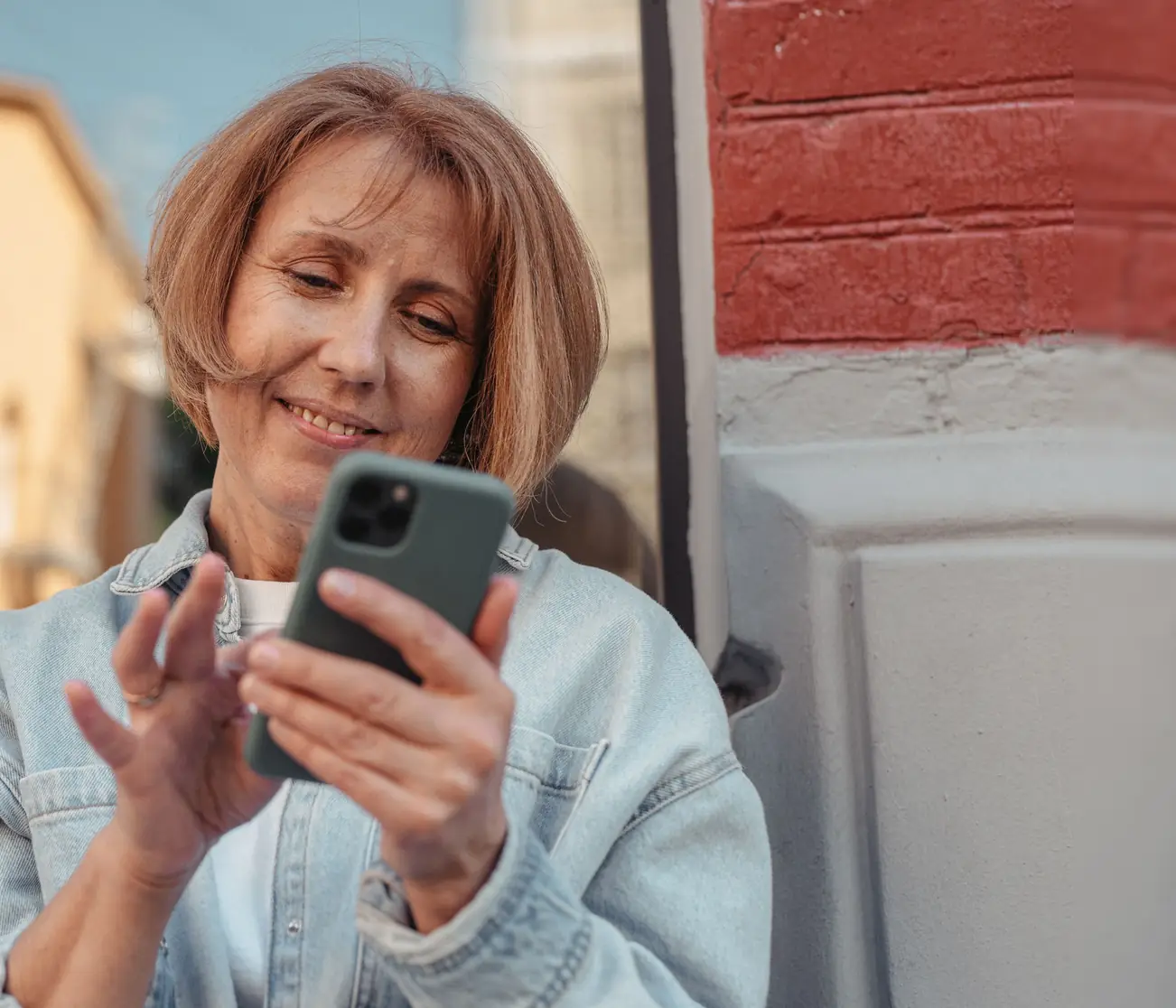 Una signora sorride mentre usa lo smartphone, all’aperto
